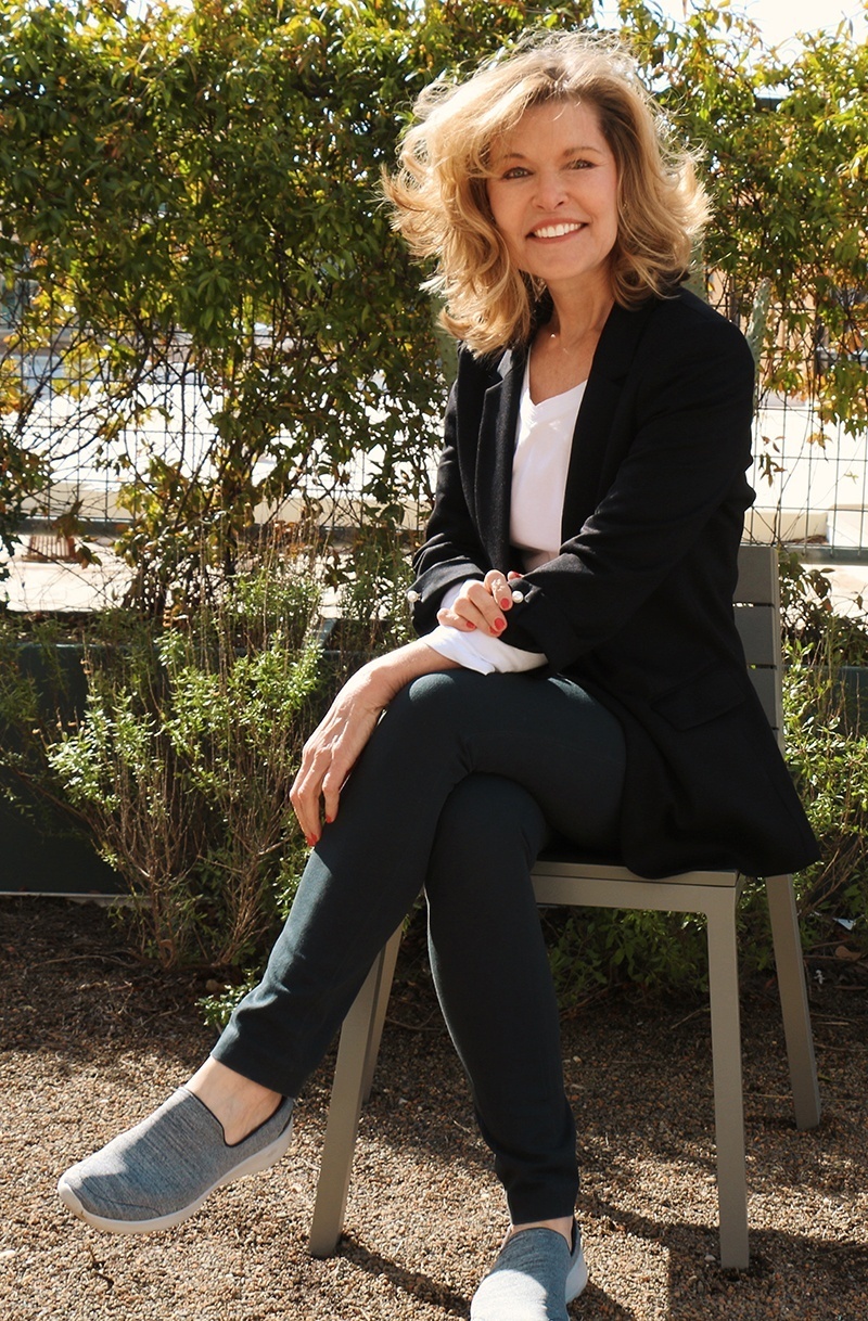 Keynote Speaker Vicki Hitzges smiles while sitting on bench in garden